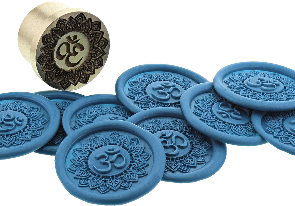 Brass wax seal stamp with Om mandala design beside blue wax seals