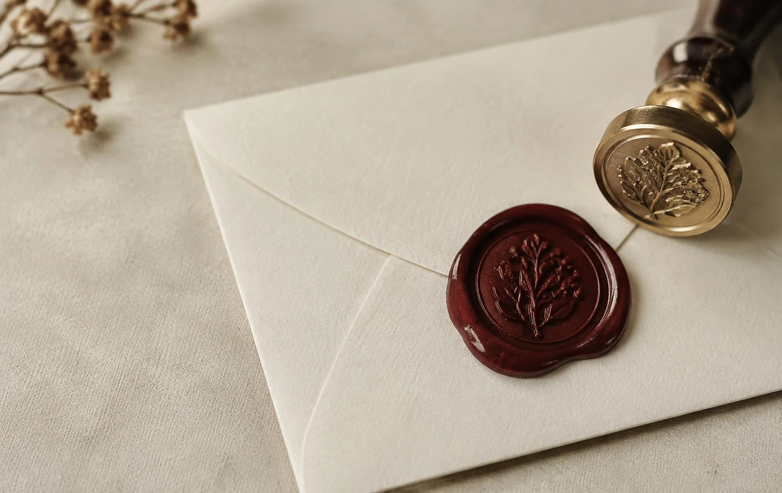 Burgundy wax seal and brass wax seal stamp on an ivory envelope